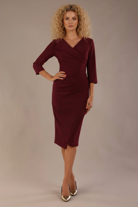 Woman wearing The Adley asymmetric draped pencil dress in rich burgundy red against a plain background (Burgundy Red)