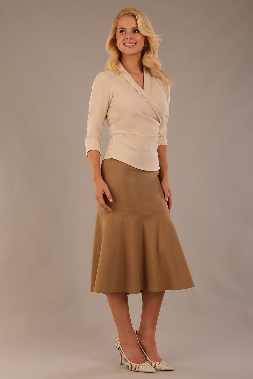 Model wearing a Trina wrap top in almond cream, with a wide V-neck and 3/4 sleeves, styled with a camel fishtail skirt.