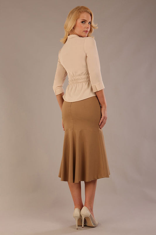 Model wearing a Trina wrap top in almond cream, with a wide V-neck and 3/4 sleeves, styled with a camel fishtail skirt.