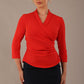 Model wearing a Trina wrap top in red, with a wide V-neck and 3/4 sleeves, styled with a navy pencil skirt.