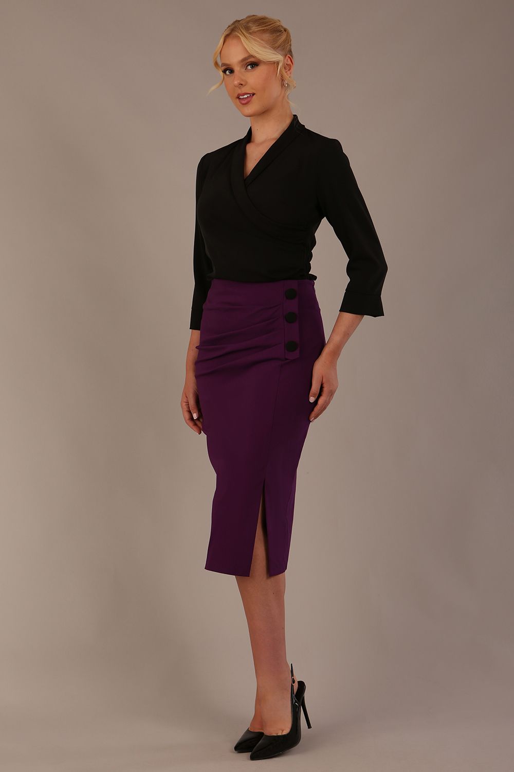 Model wearing a Trina wrap top in black, with a wide V-neck and 3/4 sleeves, styled with a purple pencil skirt.