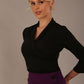 Model wearing a Trina wrap top in black, with a wide V-neck and 3/4 sleeves, styled with a purple pencil skirt close up view