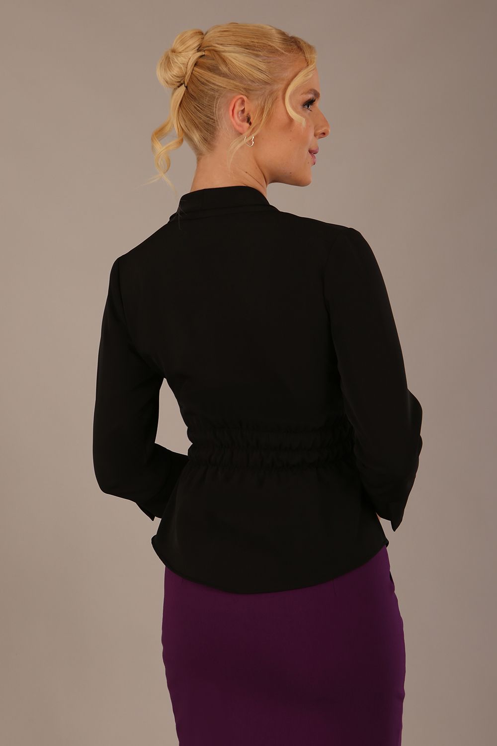 Model wearing a Trina wrap top in black, with a wide V-neck and 3/4 sleeves, styled with a purple pencil skirt back view