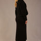 Woman wearing a black outfit with a textured jacket and the Kaden high neck midaxi dress in jet black, showing the sleek silhouette and cap sleeves against a plain background back view