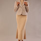 Woman wearing a beige outfit with a textured jacket and the Kaden high neck midaxi dress in cafe au lait cream, showing the sleek silhouette and cap sleeves against a plain background 