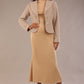 Woman wearing a beige outfit with a textured jacket and the Kaden high neck midaxi dress in cafe au lait cream, showing the sleek silhouette and cap sleeves against a plain background 