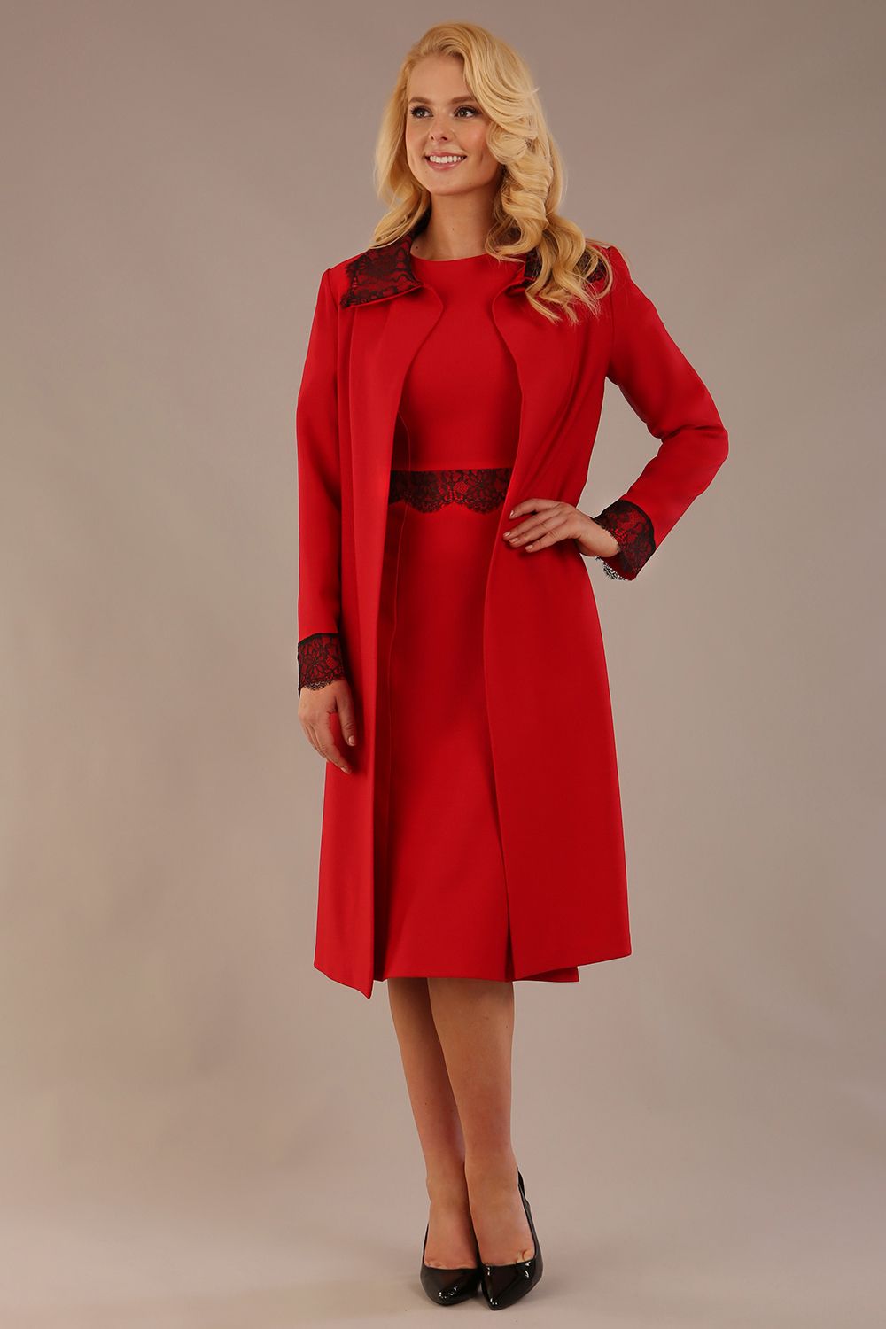 Model wearing the Lovell dress in salsa red, showcasing the fluted sleeves and black lace waistband against a beige background styled with the Haven Lace Trim Coat in the same colour