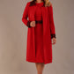 Model wearing the Lovell dress in salsa red, showcasing the fluted sleeves and black lace waistband against a beige background styled with the Haven Lace Trim Coat in the same colour