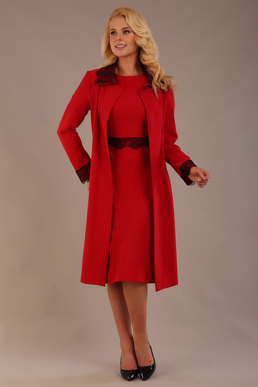 Model wearing the Lovell dress in salsa red, showcasing the fluted sleeves and black lace waistband against a beige background styled with the Haven Lace Trim Coat in the same colour