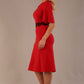 Model wearing the Lovell dress in salsa red, showcasing the fluted sleeves and black lace waistband against a beige background