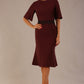 Model wearing the Lovell dress in port royale, showcasing the fluted sleeves and black lace waistband against a beige background