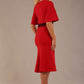 Model wearing the Lovell dress in salsa red, showcasing the fluted sleeves and black lace waistband against a beige background back view