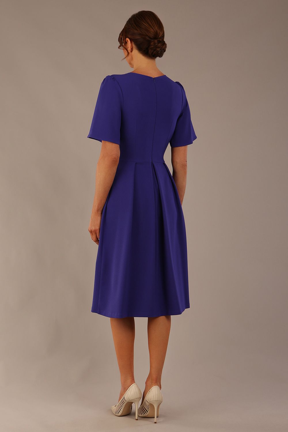 Back view of the Model wearing the Dale pleated A-line dress against a plain background (Spectrum Indigo)