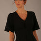 Close-up of the Model wearing the Dale pleated A-line dress against a plain background (Black)