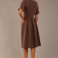 back view of Model wearing the Dale pleated A-line dress against a plain background (Peppercorn Brown)