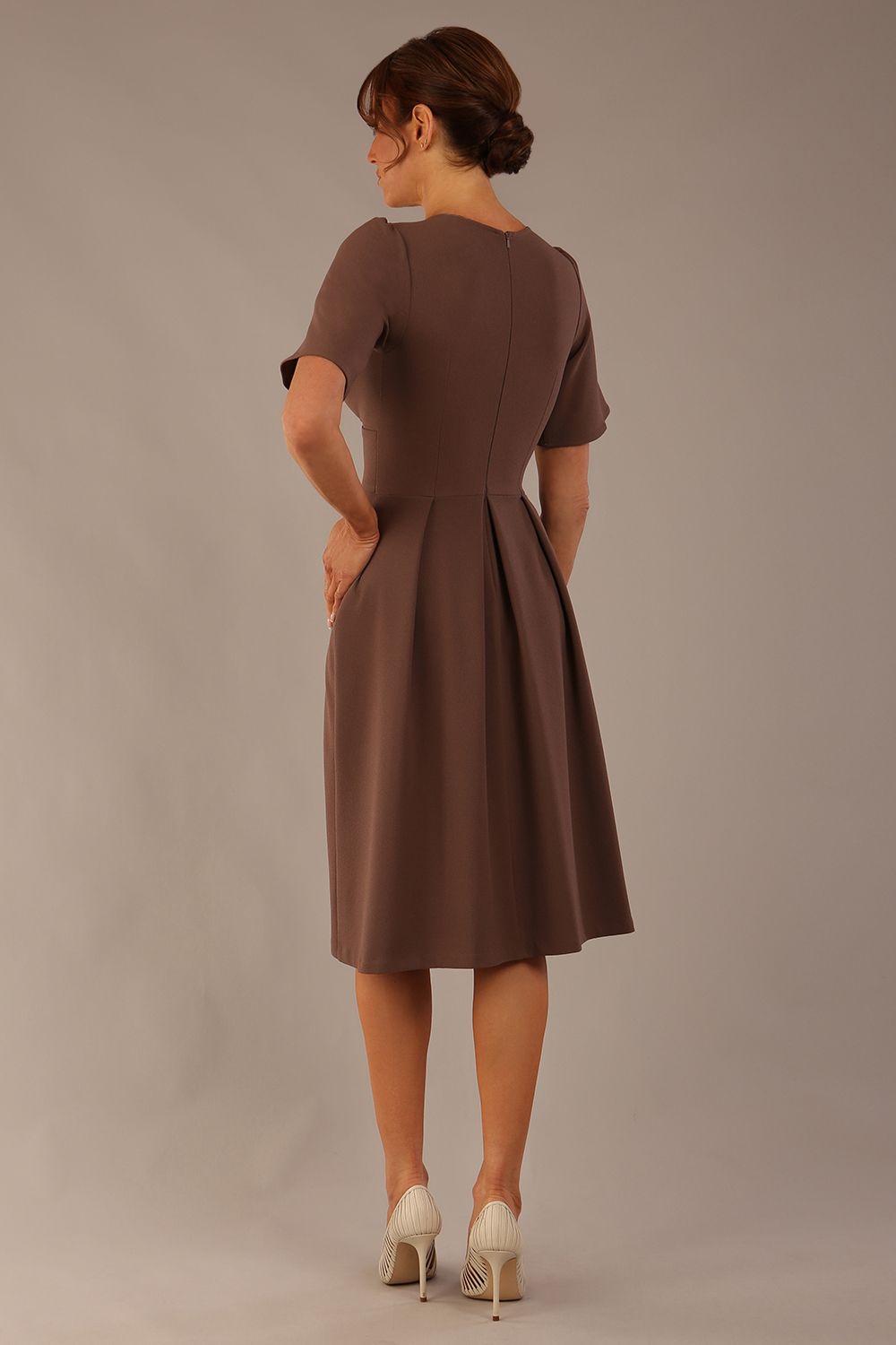 back view of Model wearing the Dale pleated A-line dress against a plain background (Peppercorn Brown)