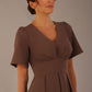 Woman wearing a brown dress against a plain background Close-up of the pleated bust detail and flared sleeves on the Dale dress in (Peppercorn Brown)