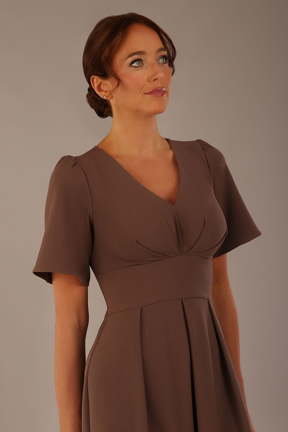 Woman wearing a brown dress against a plain background Close-up of the pleated bust detail and flared sleeves on the Dale dress in (Peppercorn Brown)