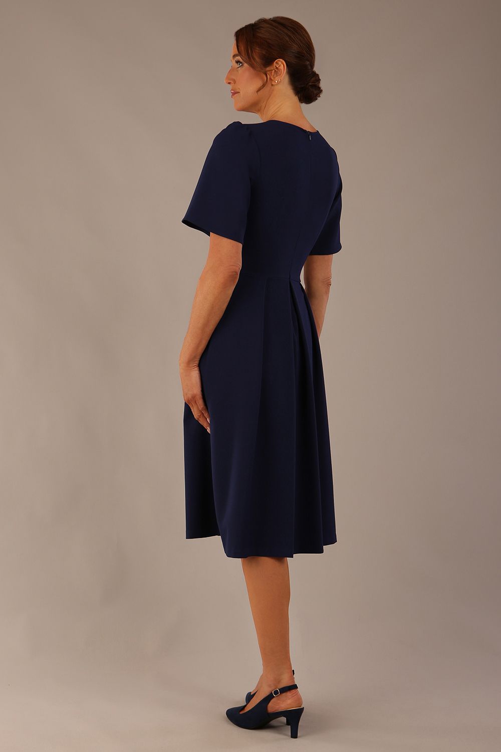 Back view of the Model wearing the Dale pleated A-line dress against a plain background (Navy Blue)