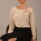 sitting model wearing a Cressida long sleeve top in almond cream, with a boat neckline and asymmetric bow, styled with a black skirt close up