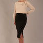 model wearing a Cressida long sleeve top in almond cream, with a boat neckline and asymmetric bow, styled with a black skirt front view