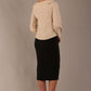 model wearing a Cressida long sleeve top in almond cream, with a boat neckline and asymmetric bow, styled with a black skirt back view