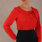 model wearing a Cressida long sleeve top in poppy red, with a boat neckline and asymmetric bow, styled with a pencil skirt close up