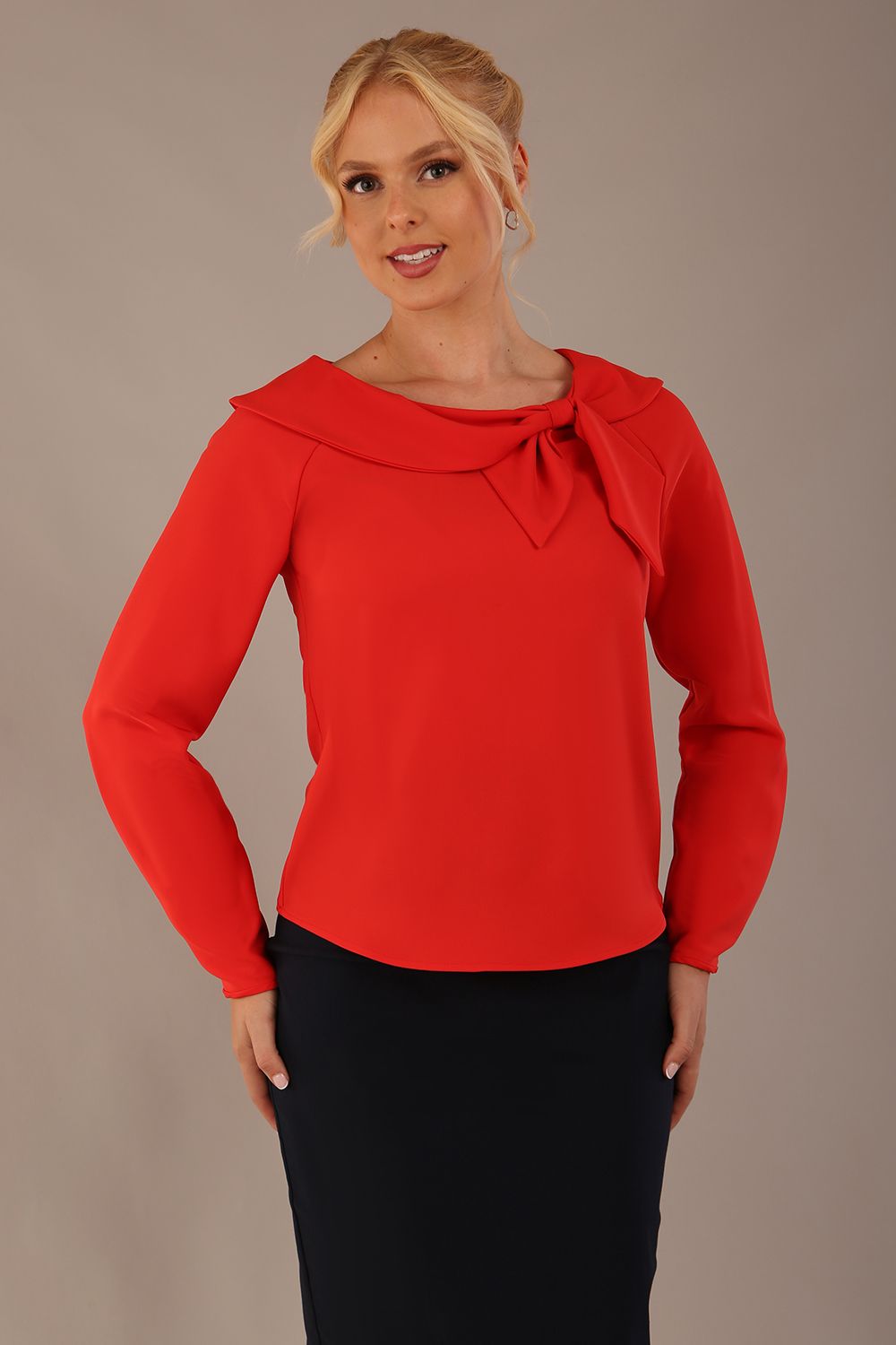 model wearing a Cressida long sleeve top in poppy red, with a boat neckline and asymmetric bow, styled with a pencil skirt front view