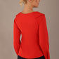 model wearing a Cressida long sleeve top in poppy red, with a boat neckline and asymmetric bow, styled with a pencil skirt back view