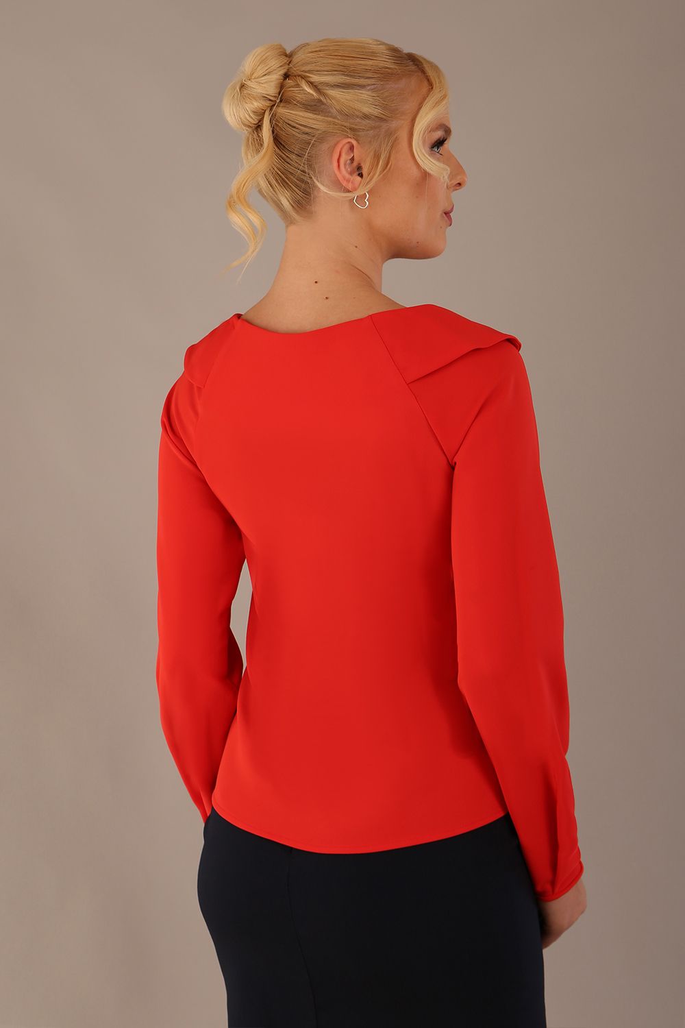 model wearing a Cressida long sleeve top in poppy red, with a boat neckline and asymmetric bow, styled with a pencil skirt back view