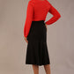 Brunette model wearing a Cressida long sleeve top in poppy red, with a boat neckline and asymmetric bow, styled with a black fishtail skirt.
