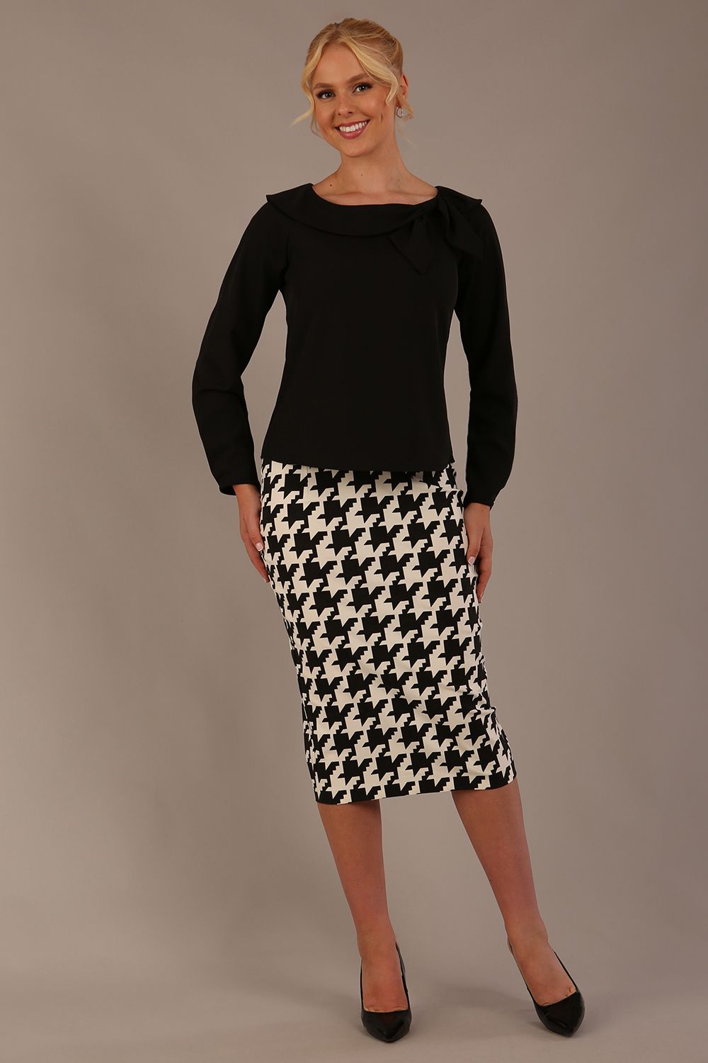 Woman wearing a diva catwalk cressida black top and houndstooth skirt against a neutral background