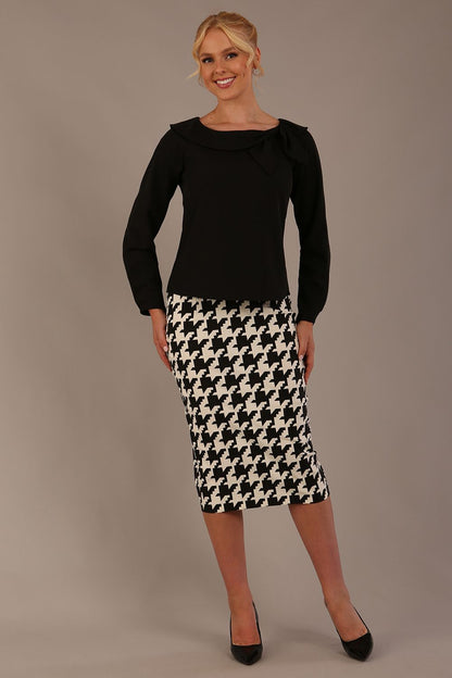 Woman wearing a diva catwalk cressida black top and houndstooth skirt against a neutral background