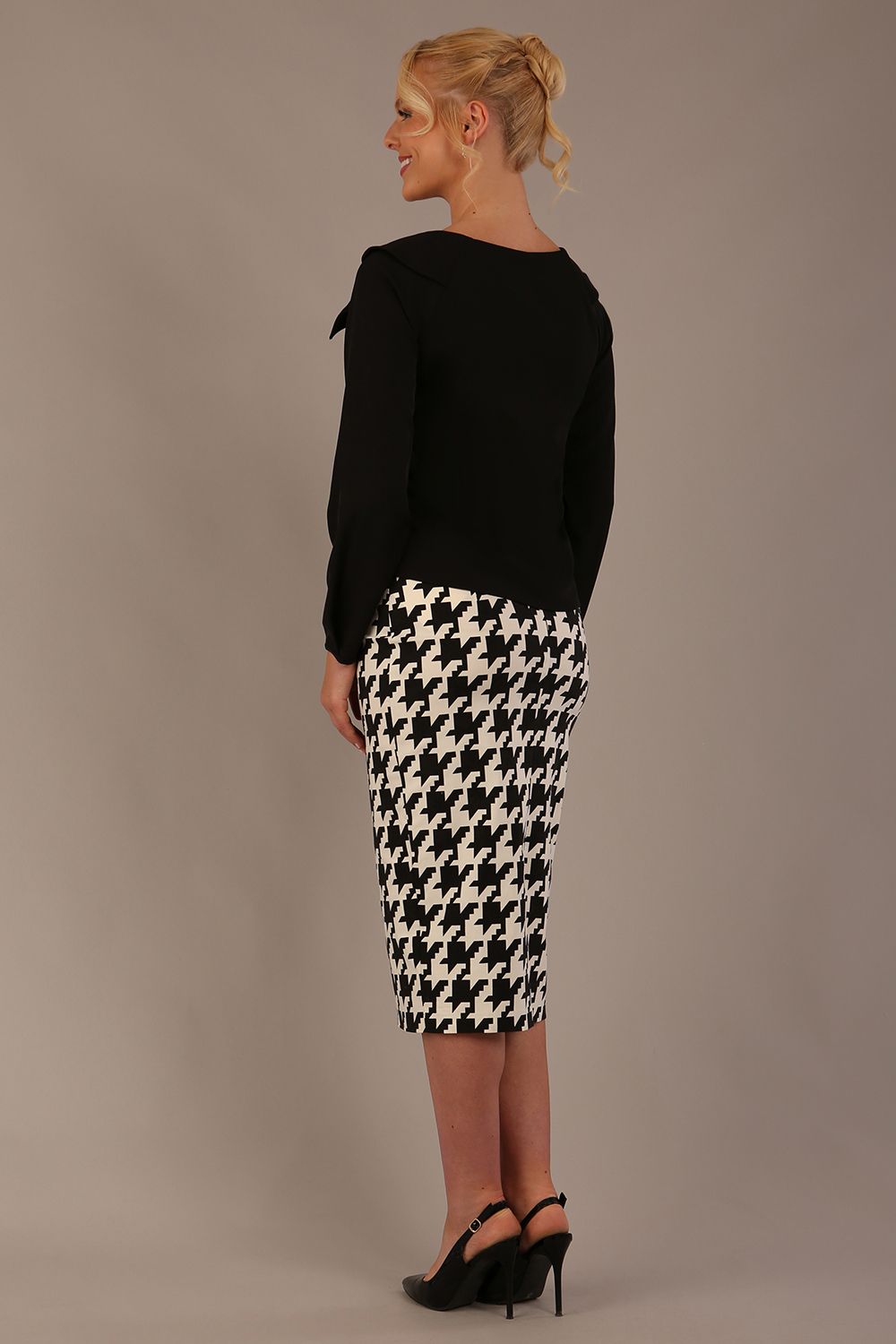 Woman wearing a diva catwalk cressida black top and houndstooth skirt against a neutral background side back view