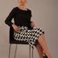 Woman sitting on a chair wearing a diva catwalk cressida black top and houndstooth-patterned skirt against a plain background