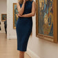 Model wearing the Wesley notched pencil dress in teal, showcasing the sculpted silhouette and V-notch neckline side view standing in an art gallery with paintings on the wall.