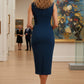 Model wearing the Wesley notched pencil dress in teal, showcasing the sculpted silhouette and V-notch neckline side view standing in an art gallery with a painting and sculpture in the background back view