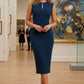 Model wearing the Wesley notched pencil dress in teal, showcasing the sculpted silhouette and V-notch neckline side view standing in an art gallery