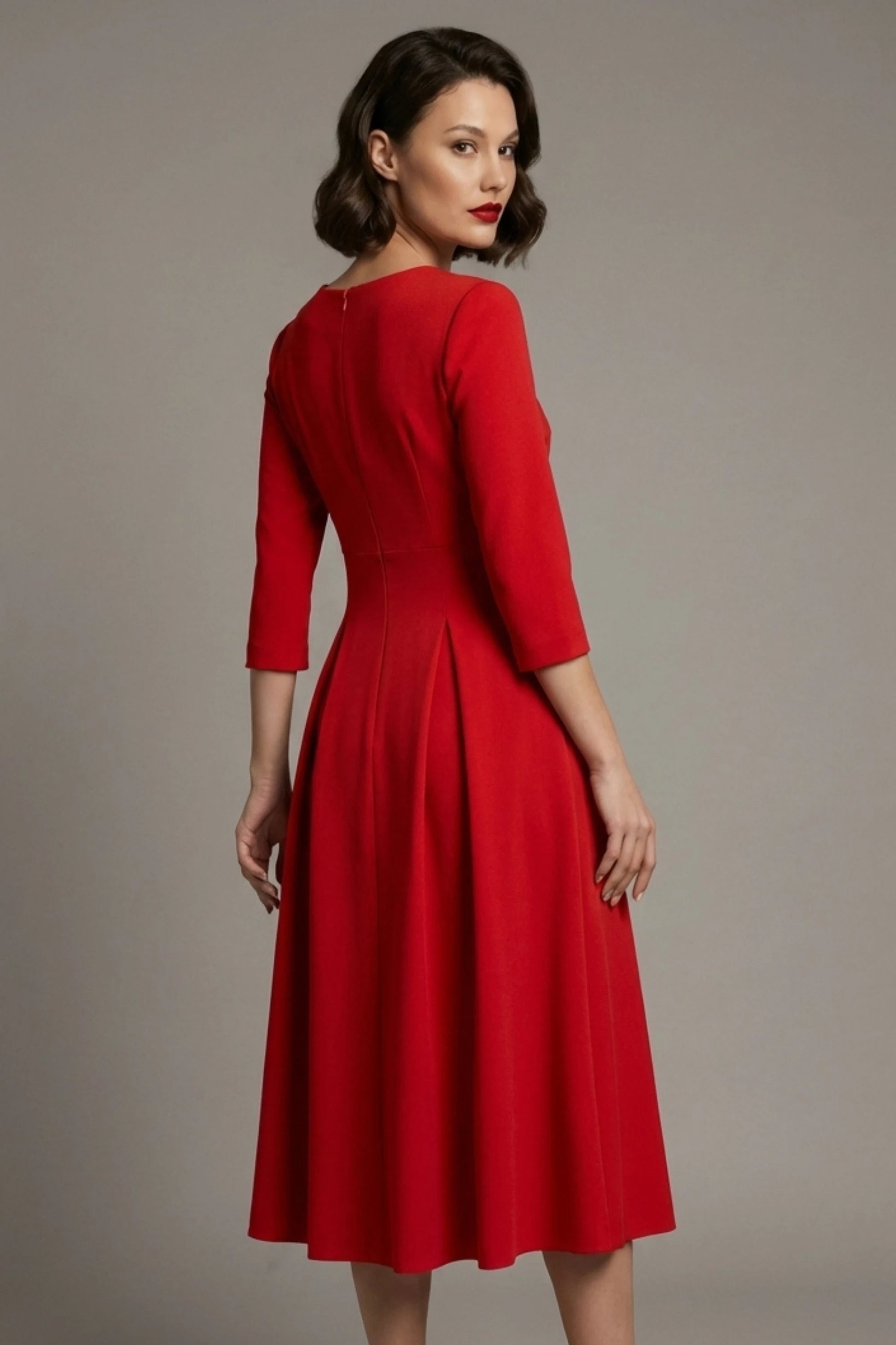 Woman wearing a diva catwalk Amanda Pleated a-line dress in a magenta pink colour against a beige background (Passion Red)