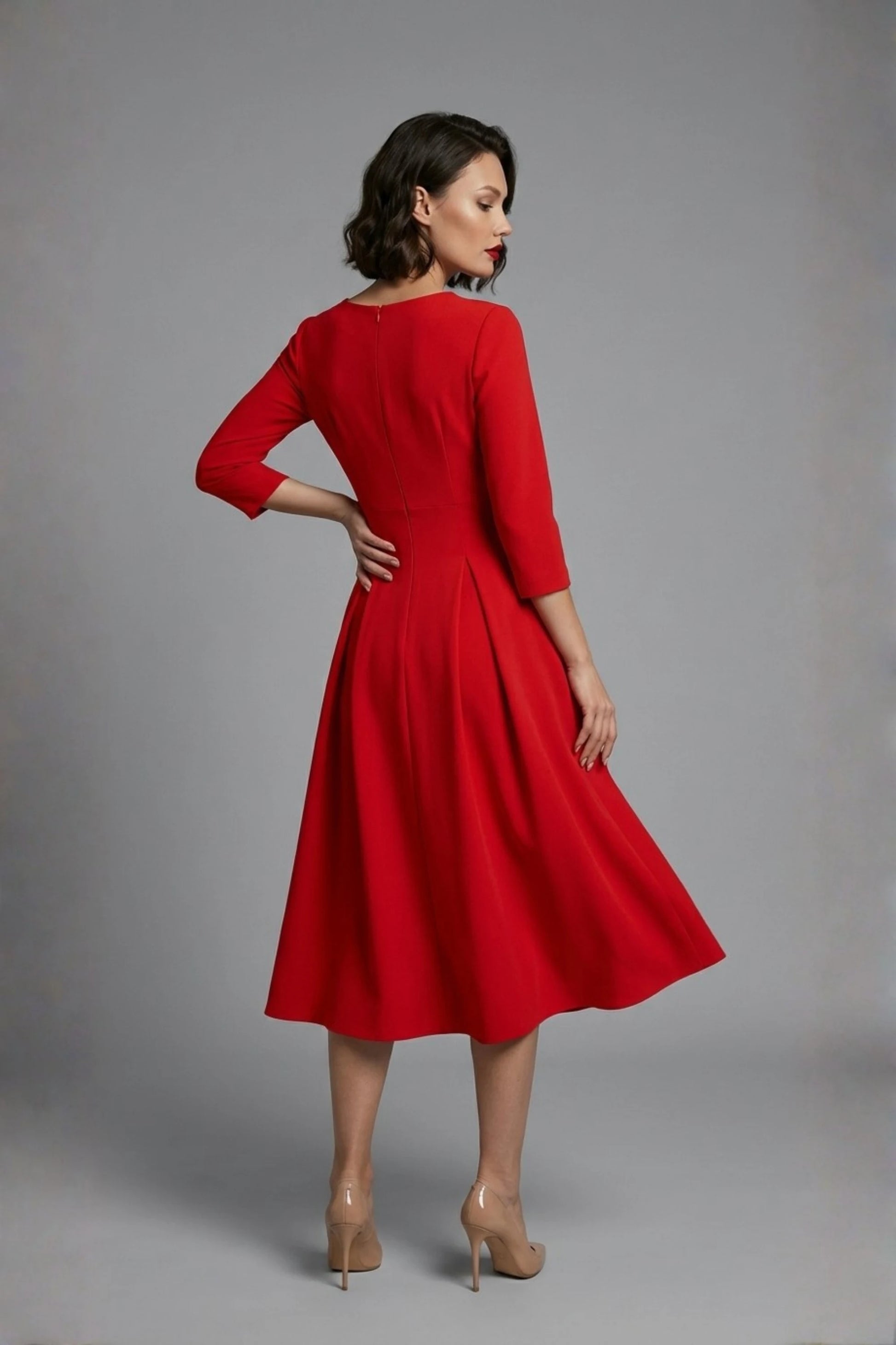 Woman wearing a diva catwalk Amanda Pleated a-line dress in a magenta pink colour against a beige background (Passion Red)