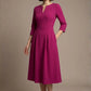 Woman wearing a diva catwalk Amanda Pleated a-line dress in a magenta pink colour with pockets against a beige background (Magenta)