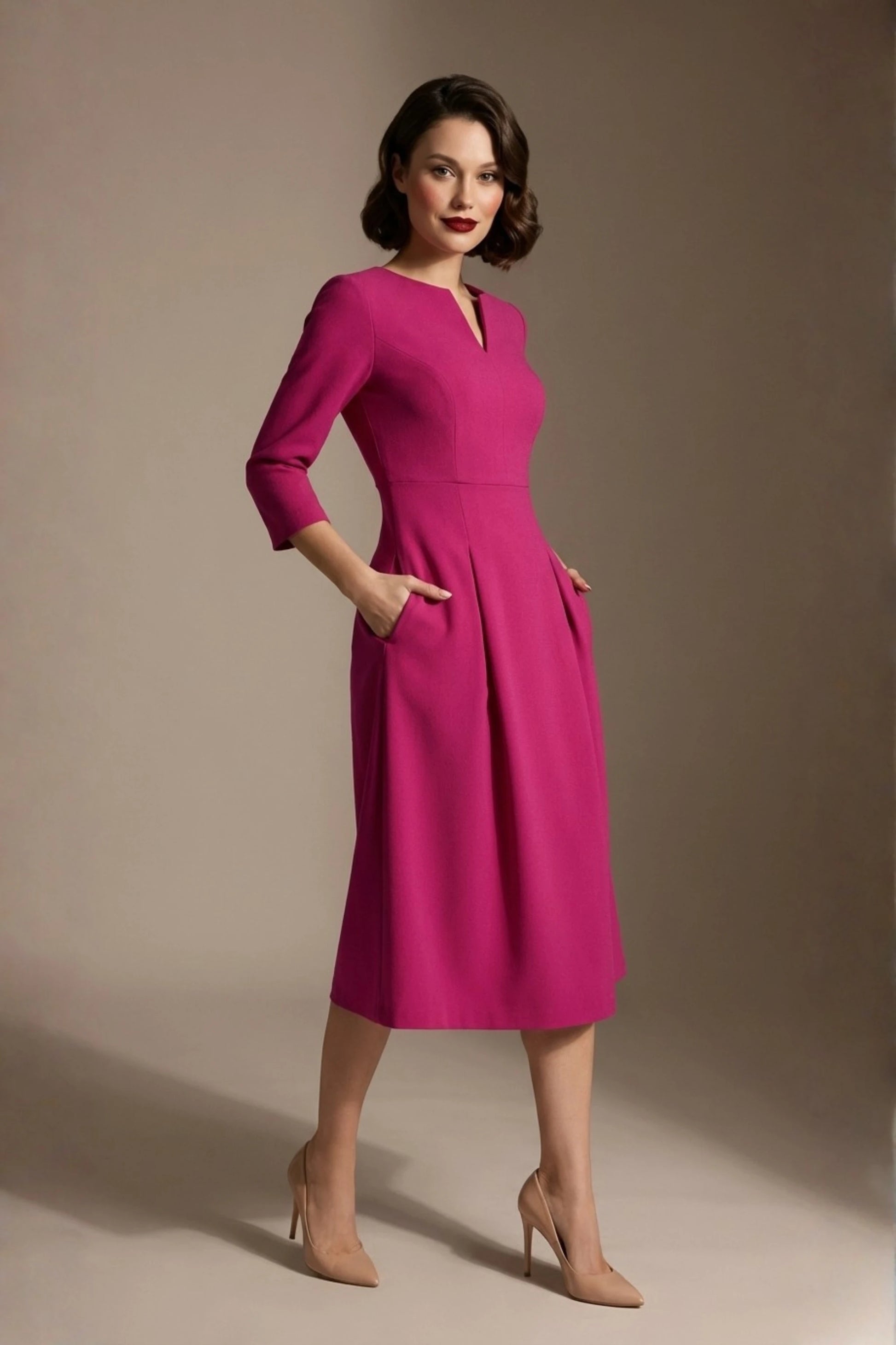 Woman wearing a diva catwalk Amanda Pleated a-line dress in a magenta pink colour with pockets against a beige background (Magenta)