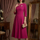 Woman wearing a diva catwalk Amanda Pleated a-line dress in a magenta pink colour standing in a room with a mirror and furniture (Magenta)