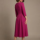 Woman wearing a diva catwalk Amanda Pleated a-line dress in a magenta pink colour against a beige background (Magenta)