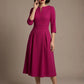 Woman wearing a diva catwalk Amanda Pleated a-line dress in a magenta pink colour against a beige background (Magenta)