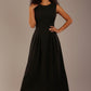 Model wearing the Cleo pleated midaxi dress in black with hands in the discreet side pockets.