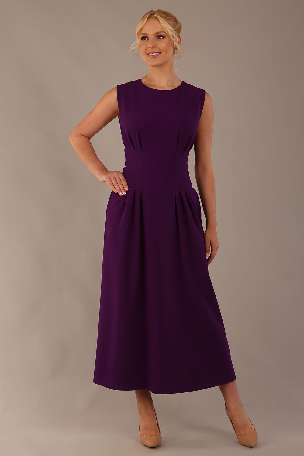 Model wearing the Cleo pleated midaxi dress in purple with hands in the discreet side pockets.