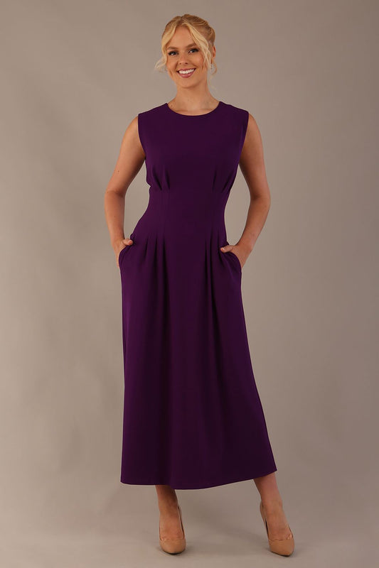 Model wearing the Cleo pleated midaxi dress in purple with hands in the discreet side pockets.