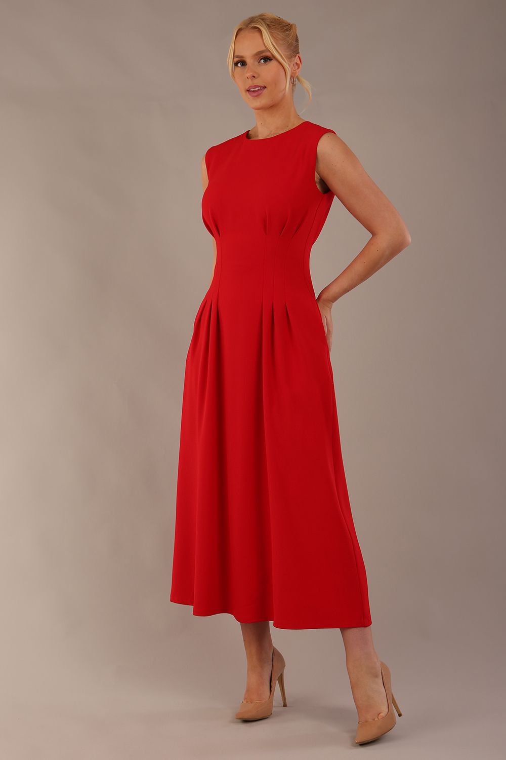 Model wearing the Cleo pleated midaxi dress in scarlet red with hands in the discreet side pockets (Scarlet Red)