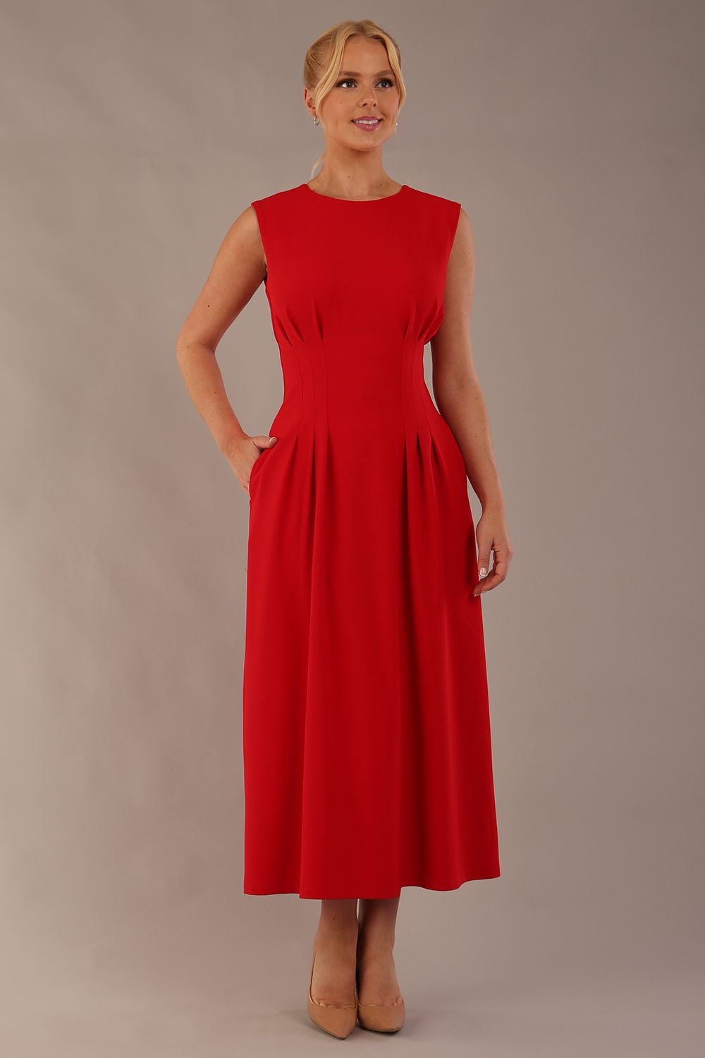 Model wearing the Cleo pleated midaxi dress in scarlet red with hands in the discreet side pockets (Scarlet Red)